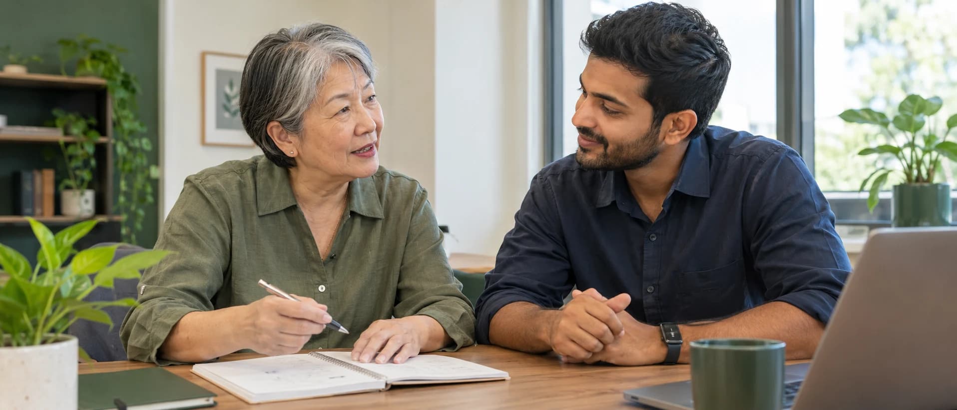 A senior professional sharing her experience with a younger colleague at a desk.
